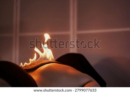 Flames Dancing on a Person's Back During a Fire Massage Therapy. A person lying down on a massage table receiving fire massage treatment. Flames are carefully placed on their back as part of this therapeutic process.