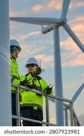 In flaming sunset clouds, two engineers on the turbine access platform check a handheld radio against the sunset high on a wind turbine access platform. Sustainable infrast photo 6630.