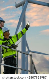 In flaming sunset clouds, two engineers on the turbine access platform compare the horizon with the radio ready high on a wind turbine access platform. Sustainable infrastr photo 6618.