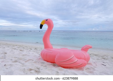 Flamingo pool float on white sand beach.