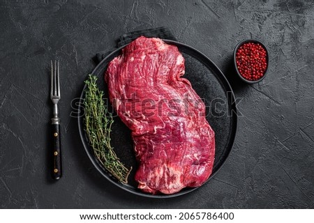 Flank or flap raw beef steak on plate with thyme. Black background. Top view.
