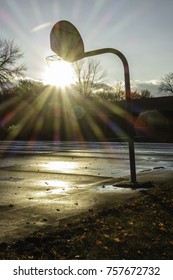 Flaring sun seems to fall through net on outdoor basketball hoop in a public park near sunset in autumn