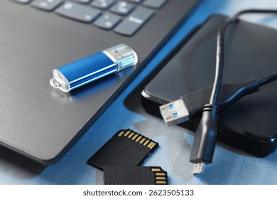 Flash drive, SD memory cards, external hard disk and laptop on gray table, closeup