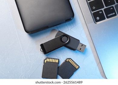 Flash drive, SD memory cards, external hard disk and laptop on light grey table, flat lay