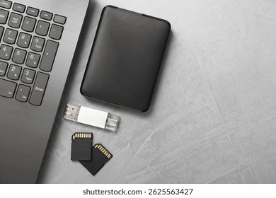 Flash drive, SD memory cards, external hard disk and laptop on gray textured table, flat lay. Space for text