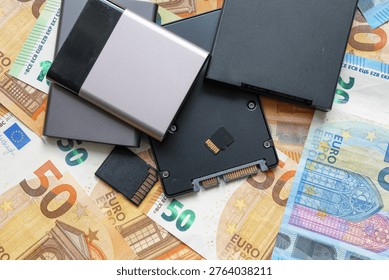 Flash drive storage devices lying on money. SSDs and memory cards on euro Banknotes. Computer and electronic equipment as subject to price increases. Top down view.