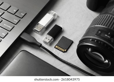 Flash drives, SD memory card, external hard disk, laptop and camera on gray textured table, closeup