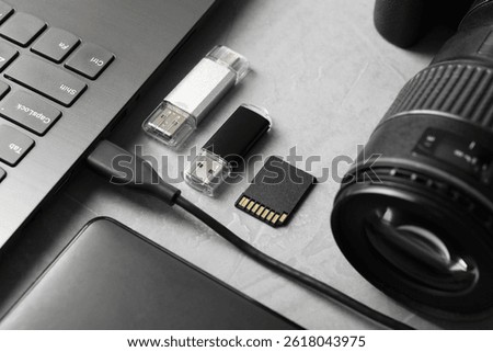 Flash drives, SD memory card, external hard disk, laptop and camera on gray textured table, closeup