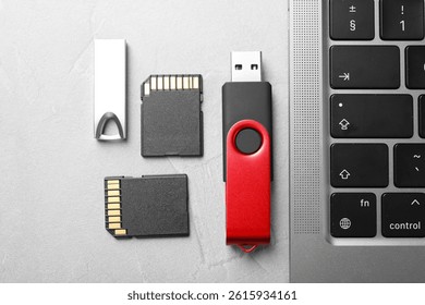 Flash drives, SD memory cards and laptop on light grey table, flat lay