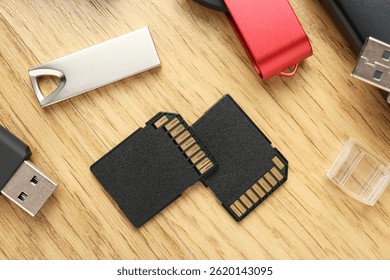 Flash drives and SD memory cards on wooden background, flat lay
