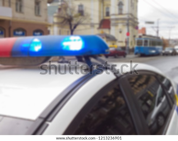 Flashing lights on the\
roof of a police patrol car on the background of a street. Abstract\
blurry image.