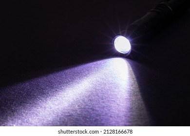 Flashlight And A Beam Of Light In Darkness. A Modern Led Lamp With Bright Projection On Dark Table. Surface With Copy Space.