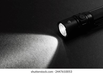 Flashlight and a beam of light in darkness. A modern led lamp with bright projection on dark wood table. Surface with copy space.