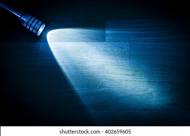 Flashlight And A Beam Of Light In Darkness. A Modern Led Lamp With Bright Projection On Dark Wood Table. Surface With Copy Space.