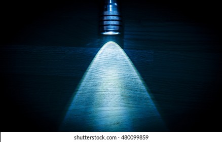 Flashlight and a beam of light in darkness. A modern led light with bright projection on dark wood table. Surface with copy space.