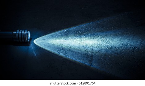 Flashlight and a beam of light in darkness. A modern led light with bright projection on dark stone surface. Surface with copy space.