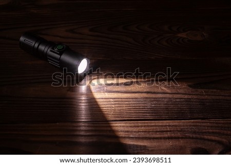Flashlight and a beam of light in darkness. A modern led lamp with bright projection on dark wood table. Surface with copy space.