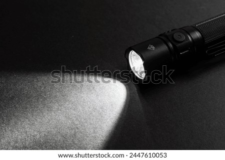 Flashlight and a beam of light in darkness. A modern led lamp with bright projection on dark wood table. Surface with copy space.