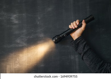 A Flashlight In A Man’s Hand And A Ray Of Light In The Dark On A Black Background. Modern LED Lamp With Bright Projection. Surface With Copy.