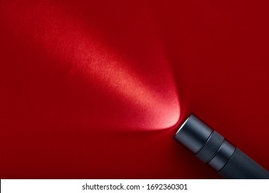 Flashlight on a red background. A beam of light from a flashlight. Finning on the metal body.