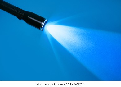 Flashlight And A Ray Of Light In The Dark On A Blue Background. A Modern LED Lamp With A Bright Projection. Surface With A Copy.