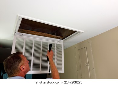 Flashlight shined into an air intake vent of a home HVAC system by an adult white male in an entryway. Adult male looking into an air intake vent with open grid after removing home HVAC air filter