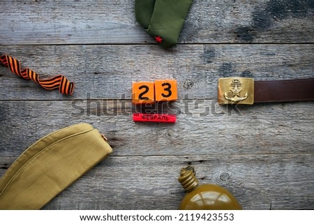 Flask, cap , george ribbon, soldier belt with a five-pointed star with a hammer and sickle and a wooden calendar with the date February 23. Fatherland defender day. Text in Russian