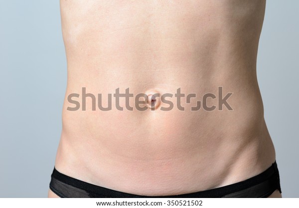 Flat Belly of a Bare\
middle-aged Slender Woman with a big belly button in Close up\
Against Gray Background.