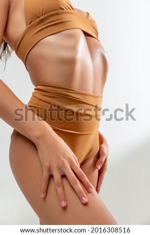 Flat belly. Cropped slim tanned female body in mustard swimsuit lstanding on white studio background. Concept of female beauty, tenderness, flexibility and self-care