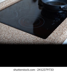 Flat built-in hob and frying pan on a marble countertop. At the bottom of the frame there is a smooth transition to a black background and a place for an inscription