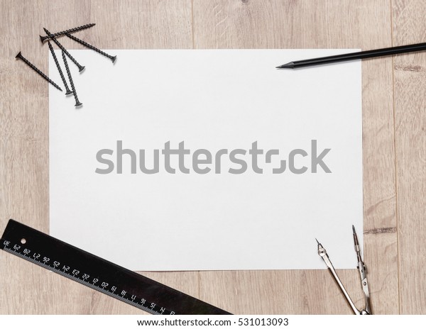 Flat composition of empty drawing sheet and\
screws, a ruler,  pencil,  compass on wooden table. Workspace\
repairman with copy space.