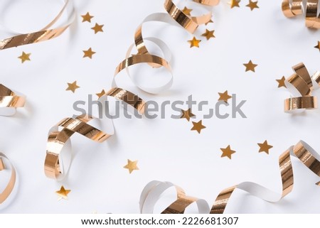 flat composition of golden ribbons or serpentine and golden confetti in the form of stars on a white background. The concept of a birthday, anniversary or holiday in golden colors.