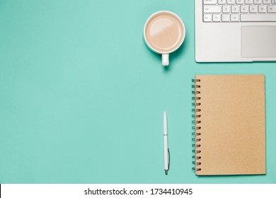 Flat composition with laptop, notebook with pen and cup of coffee or cocoa on the green mint desk. Top view. Trendy flat lay for bloggers, designers etc.