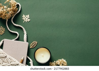 Flat lay aesthetic feminine workspace with macrame handbag, candle, dried flowers on green background. Top view cozy home, bohemian woman office desk table. Autumn, fall concept.