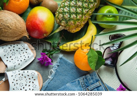 Flat Lay Arrangement Composition with Tropical Summer Fruits Pineapple Mango Bananas Coconut on Large Palm Tree Leaf. Women Jeans Shorts Slippers Hat Sunglasses. Vacation Wanderlust Travel