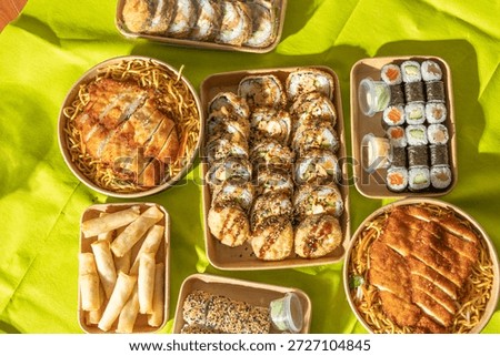 Flat lay of assorted Asian takeaway dishes including sushi rolls, fried snacks, and chicken noodle bowls. A vibrant mix of textures ideal for street food and delivery concepts.