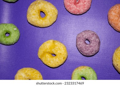 Flat lay of assorted-color sweet donuts that look delicious on a purple background.
