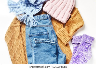 Flat Lay Autumn And Winter Fashion Photography. Stylish Women's Outfit. Brown Knitted Sweater, Blue High Waisted Mom Jeans, Pink Wool Hat, Scarf And Fluffy Socks. Trendy Comfy Clothes