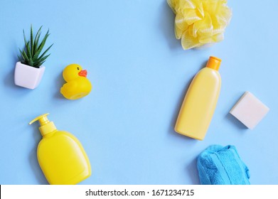 Flat Lay Baby Care Cosmetic Products. Yellow Shampoo Bottle, Liquid Soap, Sponge, Rubber Duck On A Blue Background