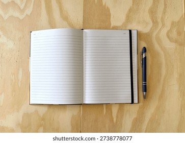 Flat Lay Of Black Notebook With White Lined Pages And An Elastic Band Place Marker Next To A Black And Silver Pen On A Light Wooden Surface
