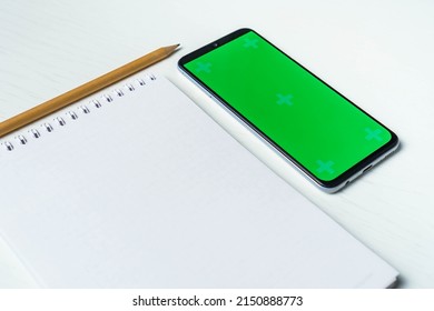 Flat Lay Of Blank Notepad With Pencil And Smartphone With Green Screen. Mockup. Todo List Concept