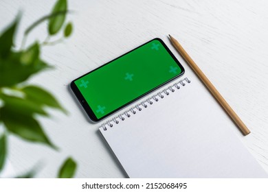 Flat Lay Of Blank Notepad With Pencil And Smartphone With Green Screen. Mockup. Todo List Concept