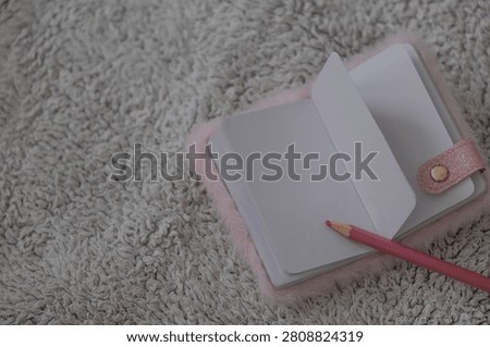 Flat lay of a blank open notebook with a pink pencil placed on a soft textured carpet. The minimalist composition represents planning, journaling, note taking, studying, creativity and personal organization. Ideal for education, productivity, stationery brands, lifestyle content and marketing materials with generous copy space. 