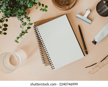 Flat lay blank paper sheet in notebook, houseplant, glass of water and other accessories on beige background. Home office desk workspace. Business, work template. Flat lay, top view.