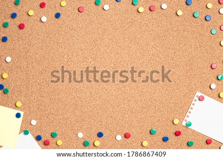 Flat lay of blank papers on a cork board with multi colored thumb tacks making a frame around the board