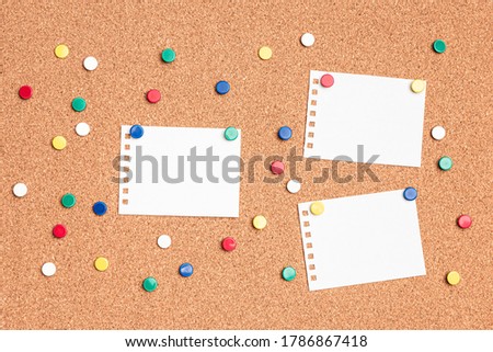 Flat lay of blank papers on a cork board with multi colored thumb tacks around