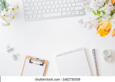 Flat lay blogger or freelancer workspace with a  keyboard, yellow tulips and branches of lilac, office supplies on a light background