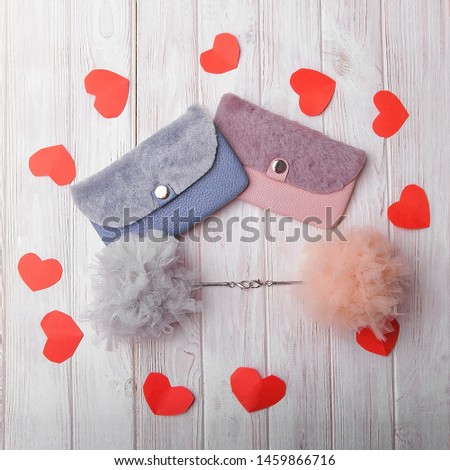 Flat lay. Blue and pink wallets, purces, clutch bags lie on white wood background with fluffy trinkets of blue and pink by. Surrounded by red origami hearts.