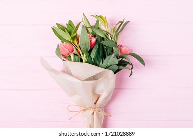 Flat Lay Bouquet Of Tulip Flowers Wrapped In Eco Brown Paper On Pink Wooden Table.