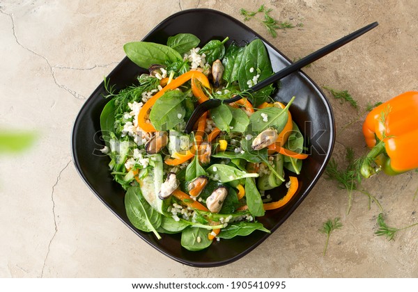 flat lay bowl of tuscan salad\
with spinach, mussels, peppers, cucumbers and bulgur on a beige\
table